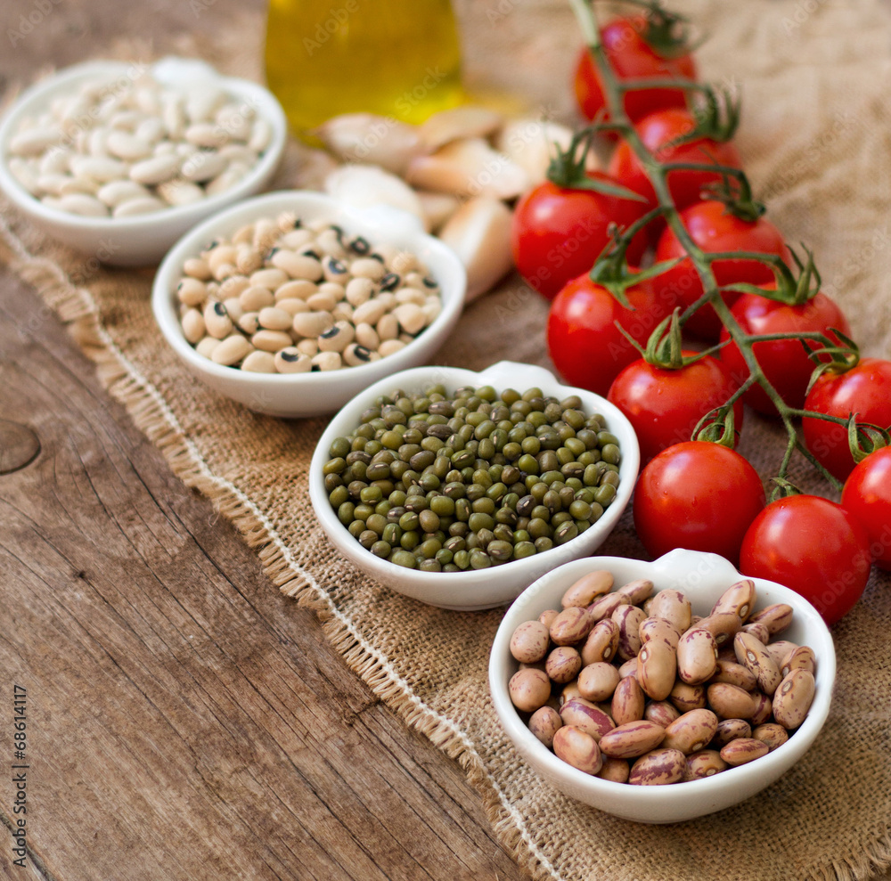 Legumes in bowls, tomatoes, garlic and olive oil on wooden table