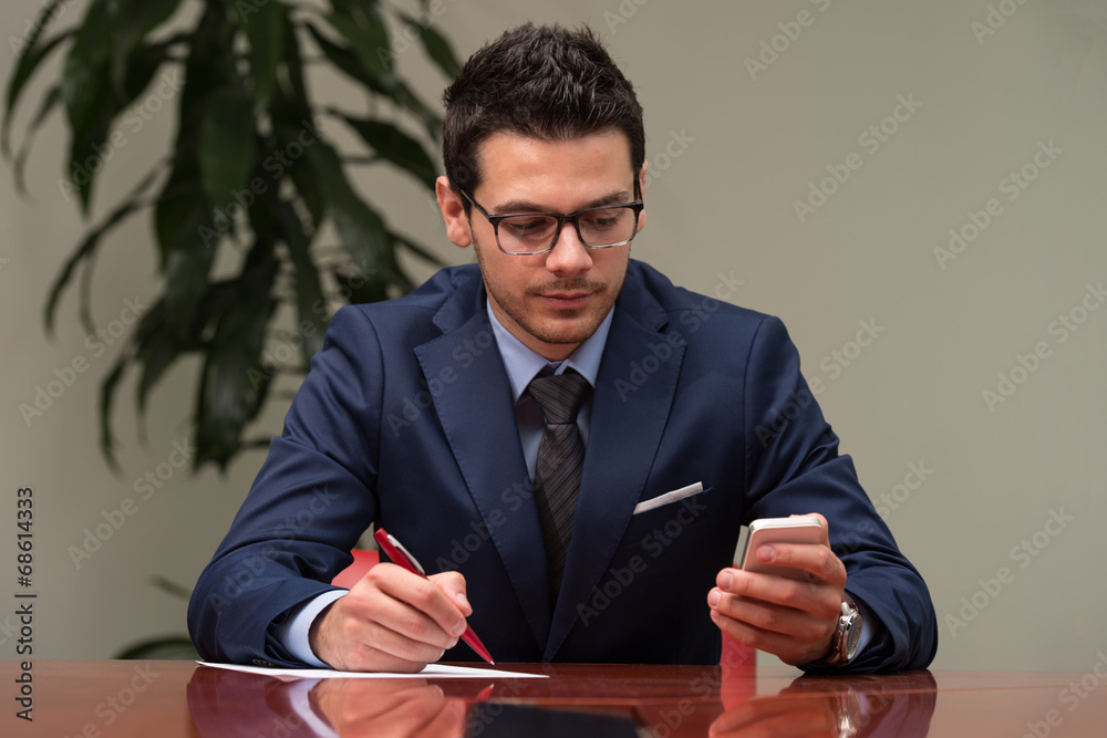 Businessman Sitting At Office Desk Signing A Contract Businessman Sitting At Office Desk Signing A Contract