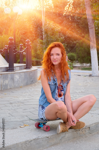 Red haired young women sitting on skateboard with her legs