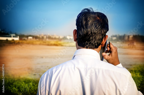 young businessman talking on smart phone facing back
