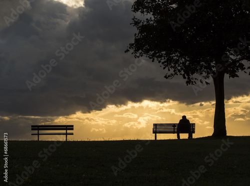 Silhouette of an anonymous man alone on a bench at sunset