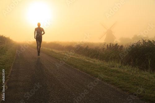 Man running in the foggy countryside near a windmill.