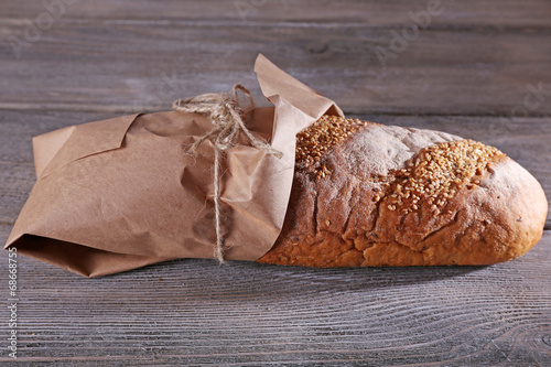 Fresh baked bread wrapped in paper, on wooden background photo