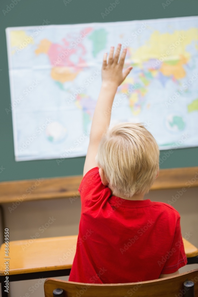 Cute pupil raising hand in classroom at his desk Cute pupil raising hand in classroom at his desk