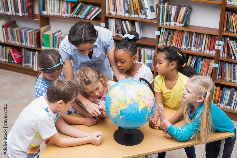 Fototapeta premium Cute pupils and teacher looking at globe in library