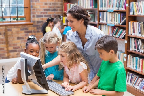 Cute pupils and teacher looking at computer in library