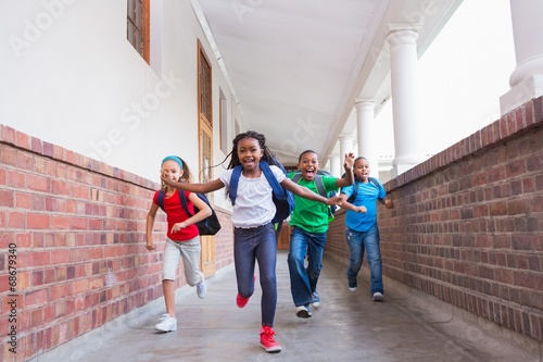 Cute pupils running and smiling at camera in hallway