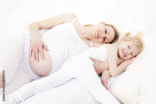 little girl with her pregnant mother resting in bed