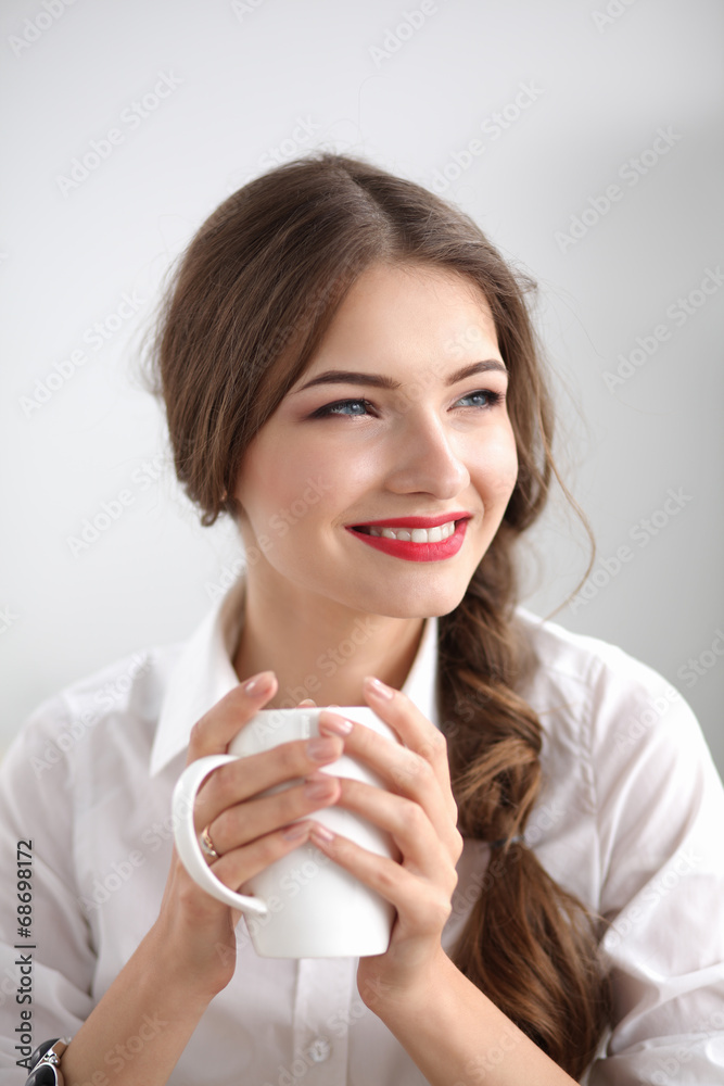Young businesswoman sitting on the desk with cup in office Young businesswoman sitting on the desk with cup in office