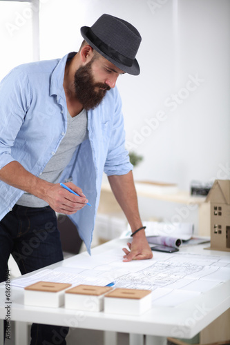 Portrait of male designer in hat with blueprints at desk