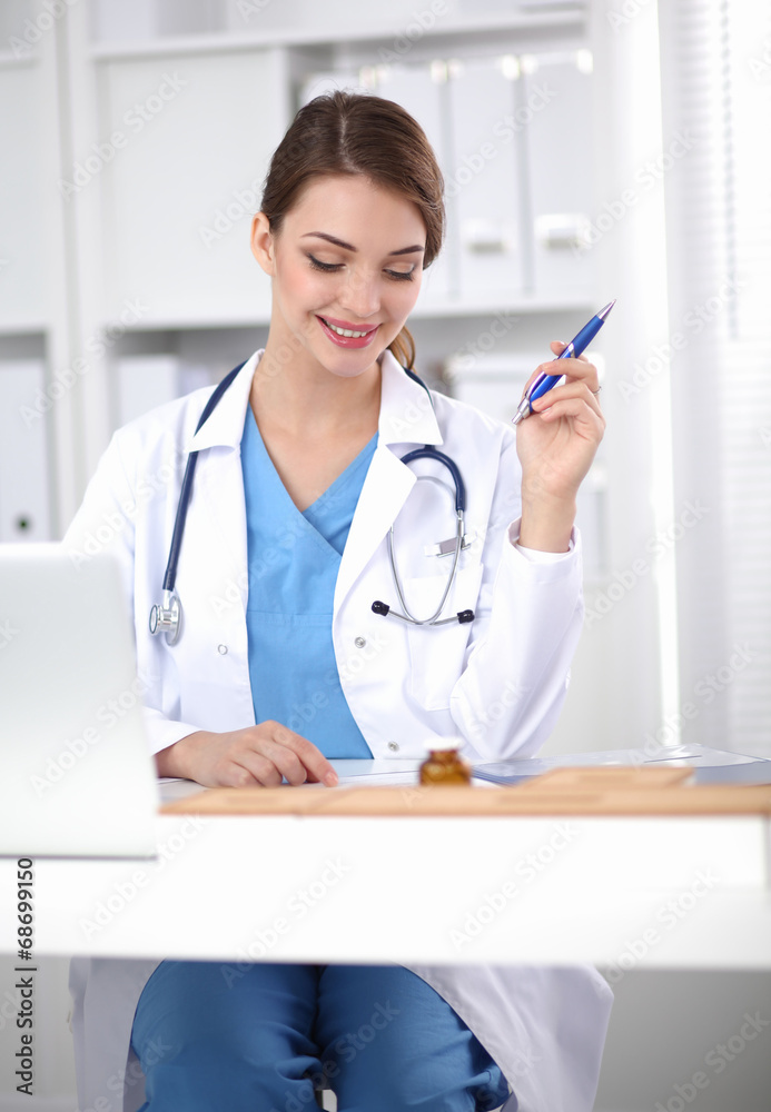 Beautiful young smiling female doctor sitting at the desk and Beautiful young smiling female doctor sitting at the desk and