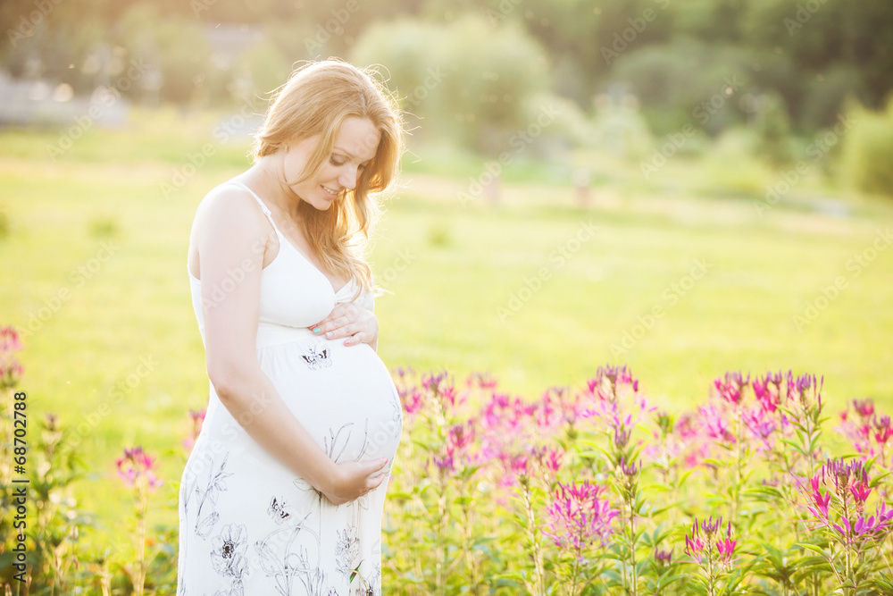 Young pregnant woman looking at her belly and smiling in park Young pregnant woman looking at her belly and smiling in park