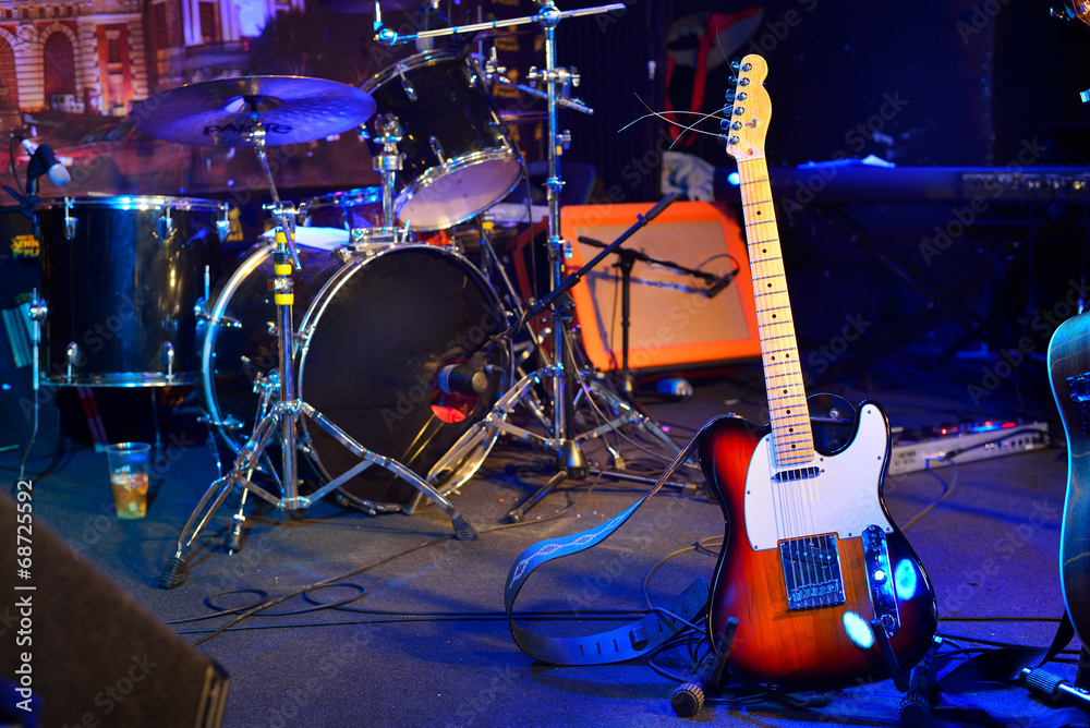 Obraz premium Electric guitar, drum kit, loudspeaker and other musical equipment on stage before concert. Neon light. Concept image. Night club, performance, music band, singing, profession, art, instrument