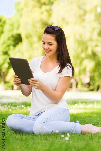 smiling young girl with tablet pc sitting on grass