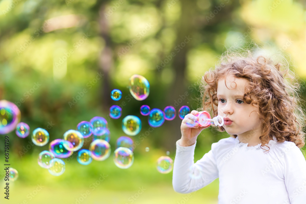 A little girl blowing soap bubbles, closeup portrait beautiful c