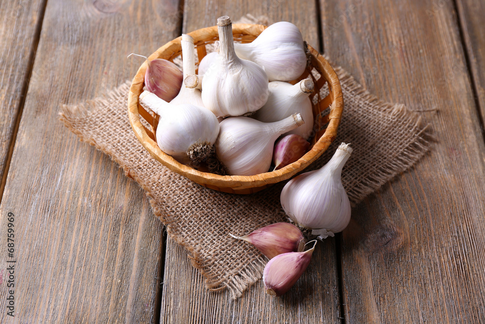 Fresh garlic in wicker basket, on wooden background