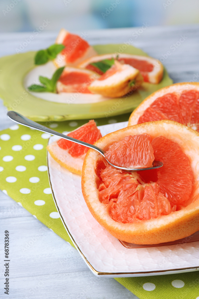 Ripe grapefruits on plate, on wooden table, on light background