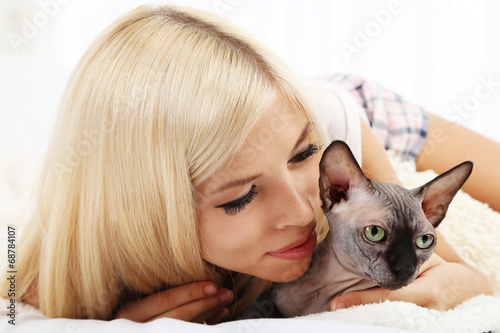 Beautiful young woman with gray sphinx cat lying on bed