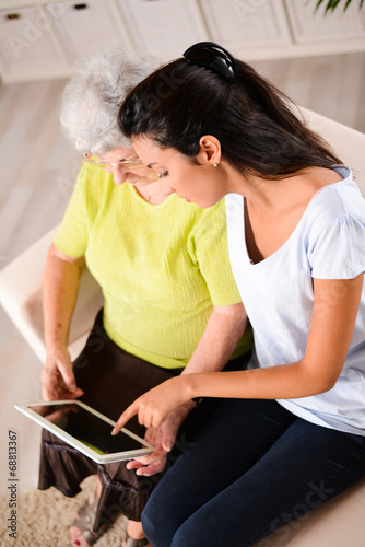 cheerful young girl with elderly woman playing with tablet home
