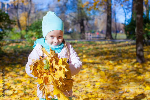 Cute little girl with yellow maple leaves outdoors at autumn