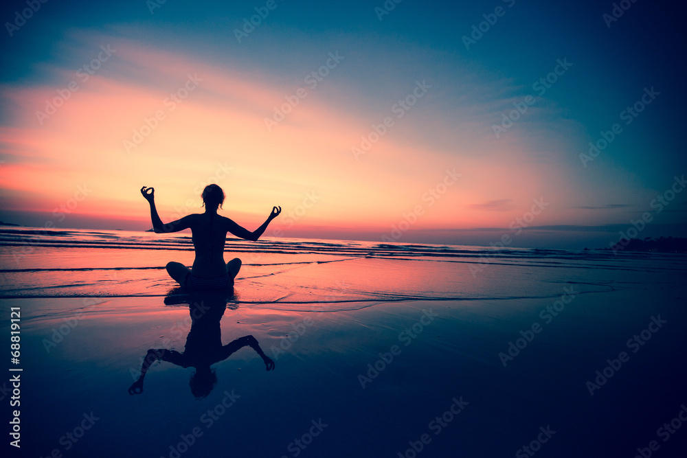 Yoga woman sitting on sea coast at surreal sunset.