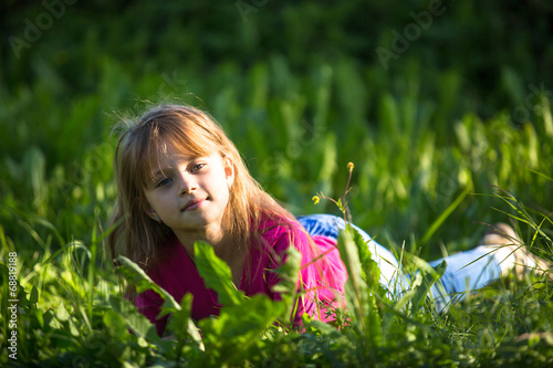 Portrait of nice little girl lying in the grass outdoors.