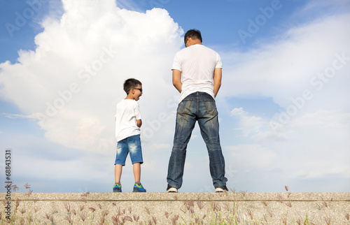 Canvas-taulu father and son standing on a stone platform and pee together