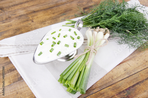 Fototapeta Naklejka Na Ścianę i Meble -  Metal bowl of cream with a tuft of onion, dill and parsley in a