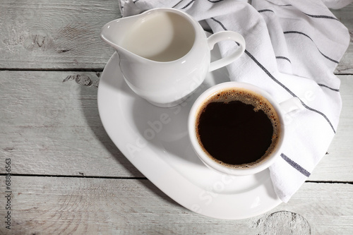Cup of coffee, creamer on color wooden background
