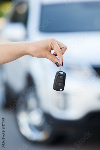 Ignition key hanging in female hand with defocused car