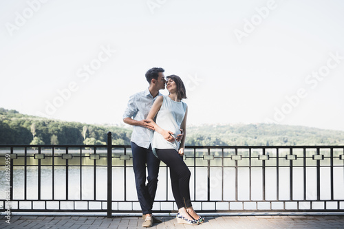 Happy and young pregnant couple hugging in nature at the lake