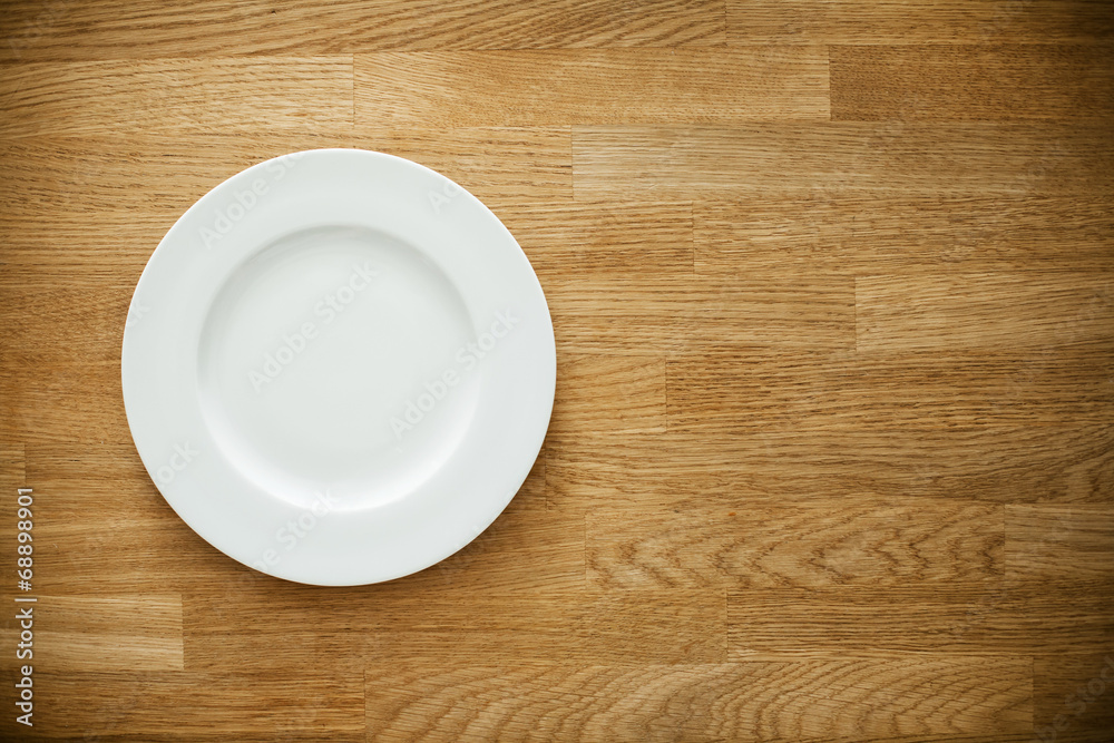 Empty white plate on wooden table Empty white plate on wooden table