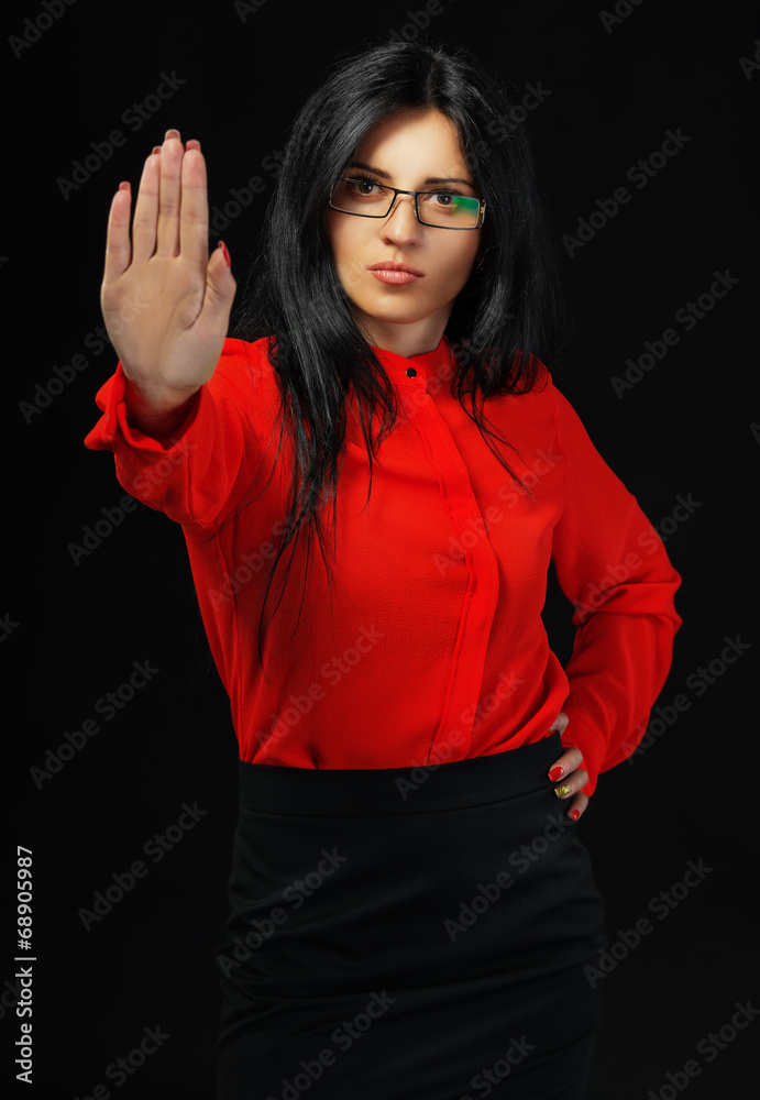 Serious business woman in red making stop sign over dark Serious business woman in red making stop sign over dark