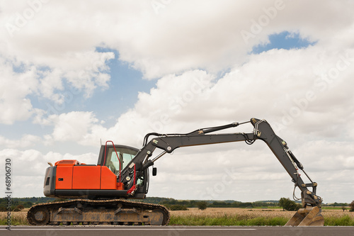 Ein grosser Bagger steht am Feldrand neben einer Strasse