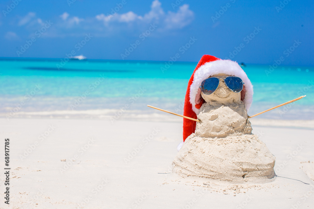 Sandy snowman with red Santa Hat on white Caribbean beach