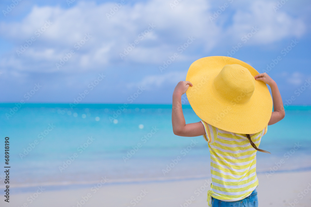 Little girl in a big yellow straw hat on white sand beach