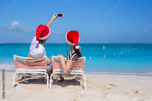 Young happy couple in red Santa hats taking a photo on cell
