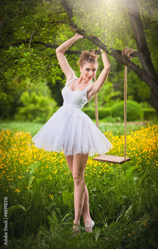 Attractive girl in white short dress posing near a tree swing