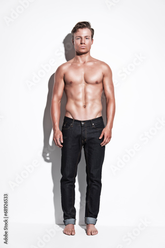 Male fitness model wearing blue jeans. Blonde hair. Against whit