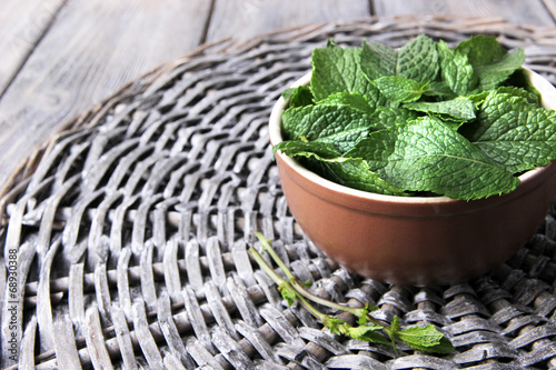 Brown round bowl of fresh mint leaves on a stand on wooden
