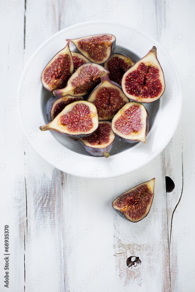 Glass plate with ripe sliced figs over white wooden background