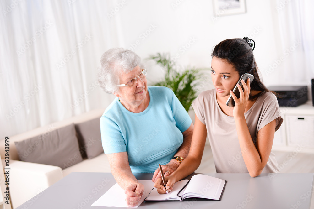 young woman helping old person for paperwork and telephone call young woman helping old person for paperwork and telephone call