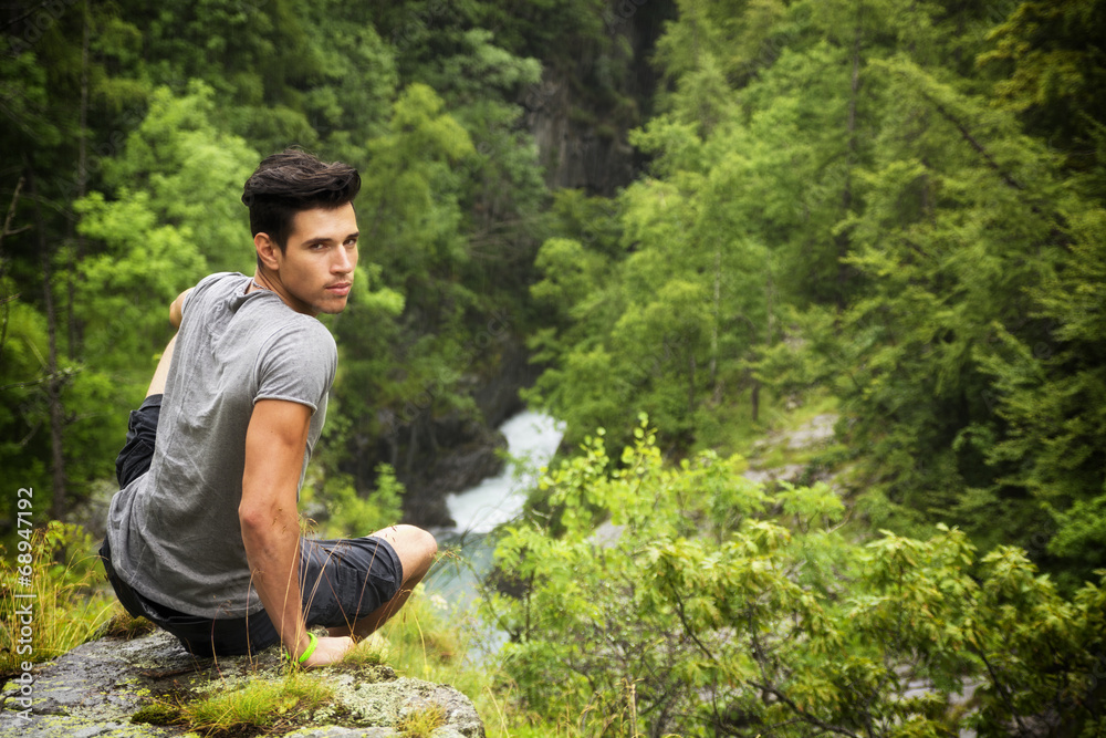 Handsome young man sitting in lush green mountain scenery Handsome young man sitting in lush green mountain scenery