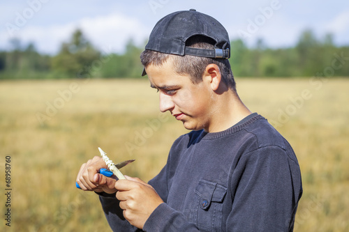 Teen with a knife cuts the branch on the field photo