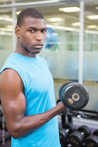 Portrait of young man exercising with dumbbell in gym