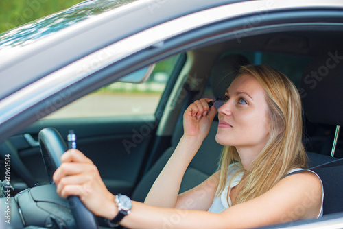 Beautiful young woman applying make-up while driving car. © M-Production
