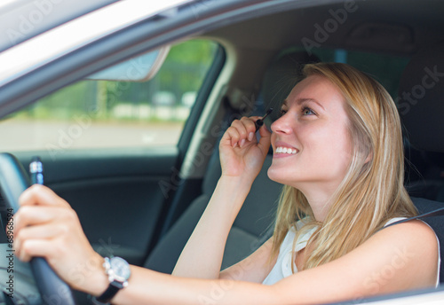 Beautiful young woman applying make-up while driving car. © M-Production