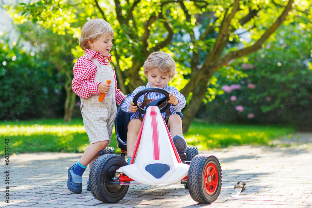 Two little sibling boys playing with pedal car in home's garden Two little sibling boys playing with pedal car in home's garden