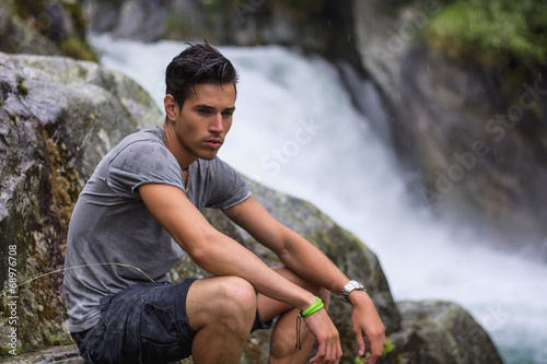 Handsome young man near mountain waterfall on rocks photo