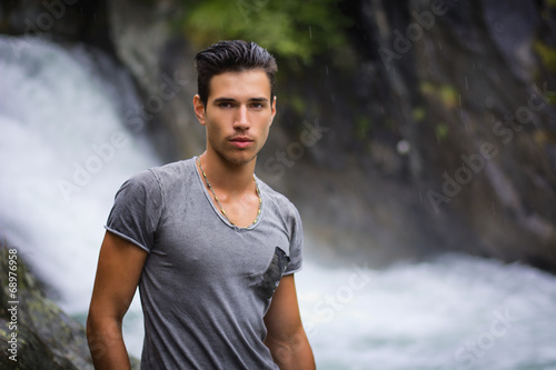 Handsome young man near mountain waterfall